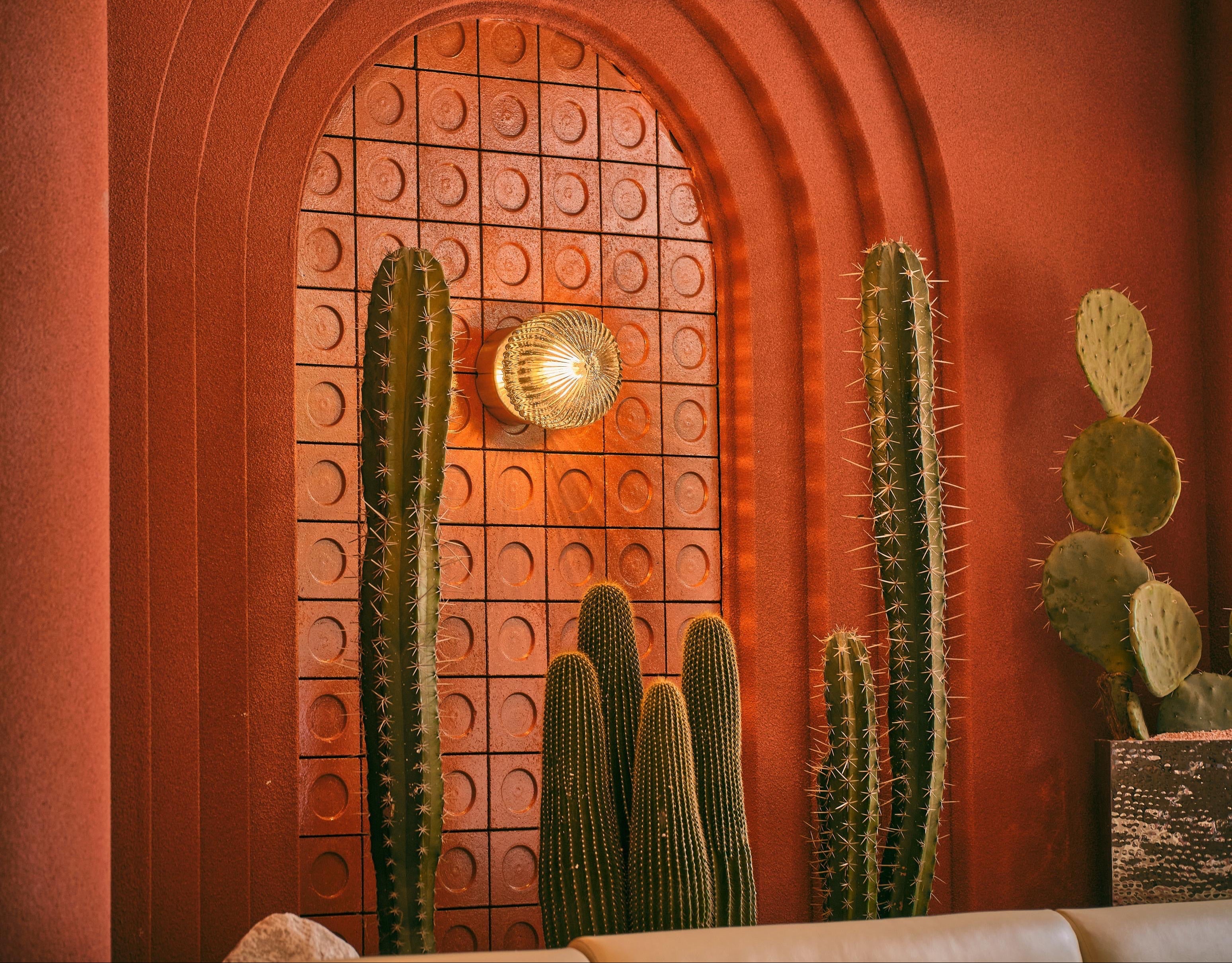 A warm, rustic interior scene with terracotta-colored arches, woven pendant lights, cacti, and a cream-colored sofa in the foreground.